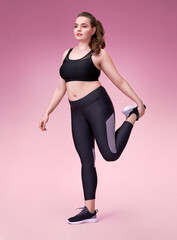 Fototapeta na wymiar Sporty woman stretching legs before workout. Photo of pretty model with curvy figure in black sportswear on pink background. Sports motivation and healthy lifestyle