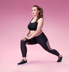 Warming up before training. Photo of pretty model with curvy figure in black sportswear on pink background. Sports motivation and healthy lifestyle
