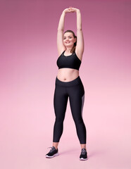 Spoty girl stretches her arms before training. Photo of pretty model with curvy figure in black sportswear on pink background. Sports motivation and healthy lifestyle