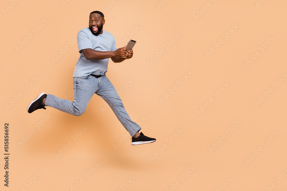 Poster full length body size view of attractive cheerful guy jumping using gadget running isolated over bei