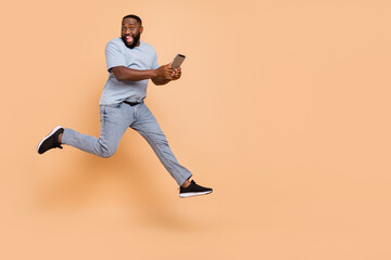 Fototapeta na wymiar Full length body size view of attractive cheerful guy jumping using gadget running isolated over beige pastel color background