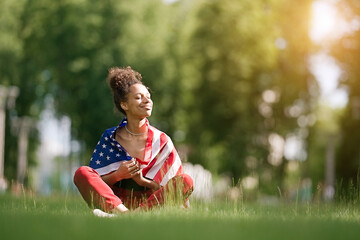 Young African american woman at nature background with an American USA flag on her shoulders. USA resident, US citizen. Immigration concept	