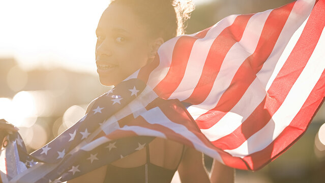 Young African american woman is waving American flag on top of at sunset background. USA resident, US citizen. Immigration concept	