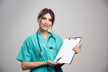 Young female doctor holding clipboard on gray background