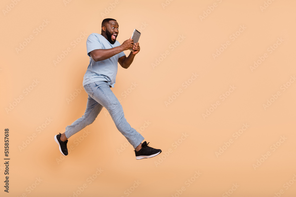 Poster full length body size view of attractive cheery guy jumping using device gadget running isolated ove