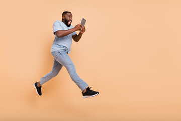 Full length body size view of attractive cheery guy jumping using device gadget running isolated...