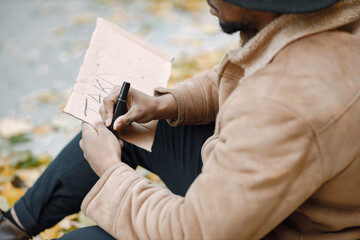 Black man sitting on a road and writing a sign for autostop