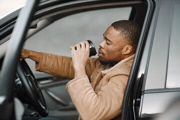Portrait of serious young black man sitting in his car and drinking a coffee