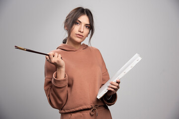 Fototapeta premium Young woman holding paint brushes and canvas