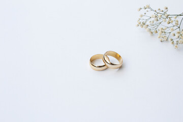 two gold wedding rings and flowers on white background.