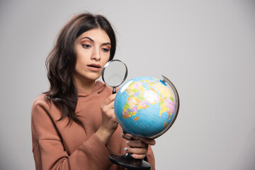 Brunette woman looking at globe with magnifying glass
