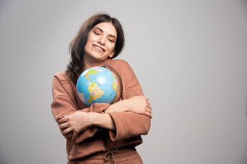 Brunette woman hugs globe on gray background