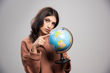 Brunette woman pointing at globe on gray background
