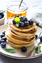 Pancakes stack with fresh blueberries and honey at white stone table.
