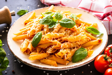 Pasta with tomato sauce, basil and parmesan on dark table. Penne pasta with tomato sauce alla arrabbiata.