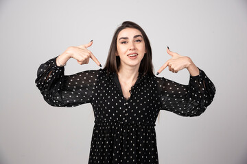 A young woman in dress pointing with two hands at herself