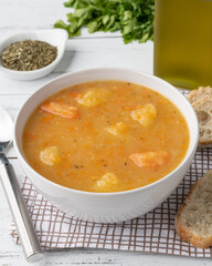 Vegetable soup in a bowl with seasonings and bread slices over wooden table