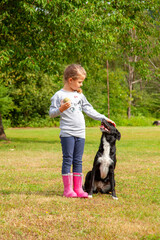 Cute little girl training her black female dog from dog shelter in summer in park