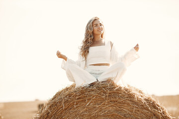 Naklejka premium Beautiful young woman in vwhite dress sitting on hay bale.