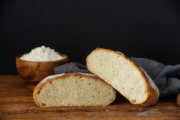 Two halves of artisan sourdough wheat bread on a linen towel on a wooden table. Homemade wheat bread cut in half
