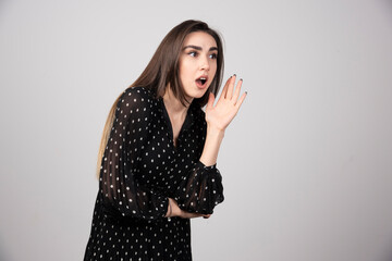 Portrait of woman calling for someone on gray background