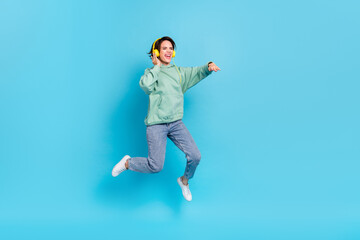 Obraz premium Full body photo of sweet young brunette lady jump wear headphones pullover jeans sneakers isolated on blue background