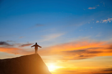 Silhouette of young hikers standing on the rock on top of the mountain mountains with rising hands at sunrise and beautiful sky background.