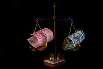 Banknotes in denominations of 100 American dollars and 100 Chinese yuan on the scales on a black background