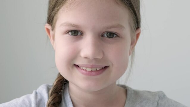 Headshot portrait of smiling little girl isolated on grey background. Child looking at camera, happy small elementary school pupil in gray t-shirt posing feel overjoyed