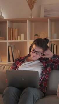 Vertical video. Fun online weekend. Cozy home evening. Internet entertainment. Joyful laughing woman enjoying watching comedy movie on laptop on couch in living room.