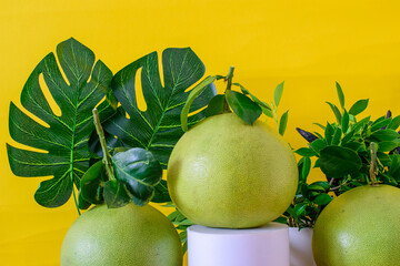 Tropical fruit grapefruit on a pedestal decorated with monstera leaves on a yellow background...