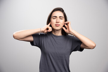 Fototapeta premium Young woman covering her ears over a gray background