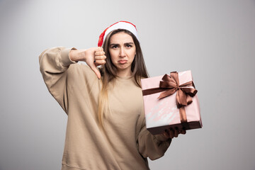 Young woman holding a Christmas present and showing a thumb down