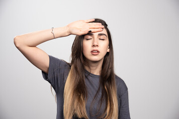 Fototapeta premium Portrait of young woman touching her forehead posing over gray background