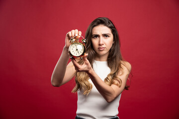 Young woman showing an alarm clock on a red background