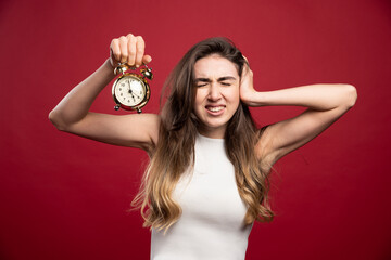 Young woman holding an alarm clock on a red background