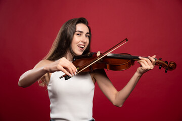 Fototapeta premium Young beautiful woman playing the violin on a red background