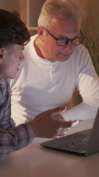Vertical video. Father son movie. Weekend family leisure. Internet fun. Shocked young guy watching weird show with confused surprised mature dad on laptop at home.