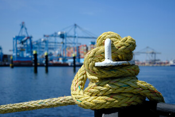 A iron bollard with a tied rope on a quay in the Port of Rotterdam in the Netherlands. In the background, slightly out of focus, is the industrial area of the Maasvlakte near Rotterdam.