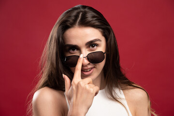 Fototapeta premium Young pretty woman putting on glasses and posing on a red background