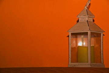 Mała latarenka na świeczkę stojąca na drewnianej półce na pomarańczowym tle .
