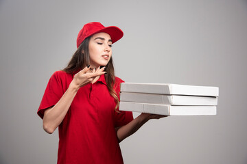 Delivery woman smells hot pizzas on gray background