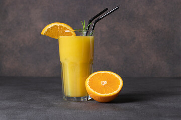 Fresh orange juice in a tall glass with a sprig of rosemary on dark background