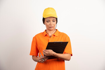 Serious woman courier with pencil looking on clipboard on white background