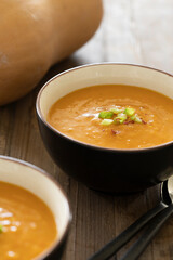 Side view of bowl with delicious pumpkin soup, ingredient like pumpkin and spoons on a wooden table