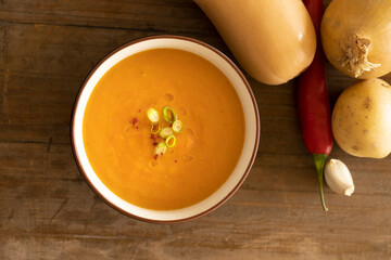 Top view of bowl with delicious pumpkin soup, ingredients like pumpkin, potato, garlic and pepper on a wooden table