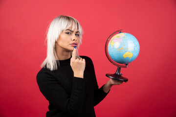 Young woman posing with a globe on a red background