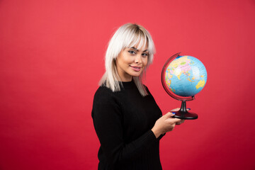 Young woman posing with a globe on a red background