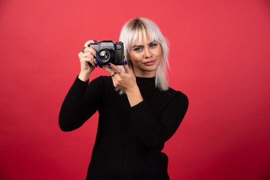 Young woman taking pictures witha camera on a red background
