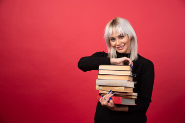 Young woman model carrying a lot of books on a red background
